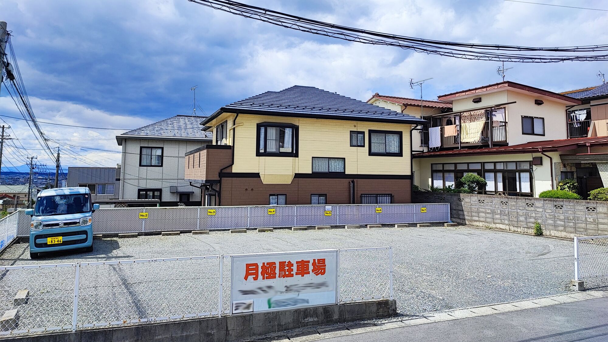 A residential area with houses, a parked car, and a sign indicating a parking lot.