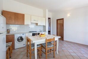 Une cuisine compacte équipée d’un lave-linge, de meubles en bois, d’un pare-feu en carrelage et d’une table à manger avec des chaises.
