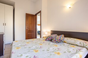 Une chambre à coucher avec un lit, des oreillers, une table de chevet, une lampe, une armoire et une porte.