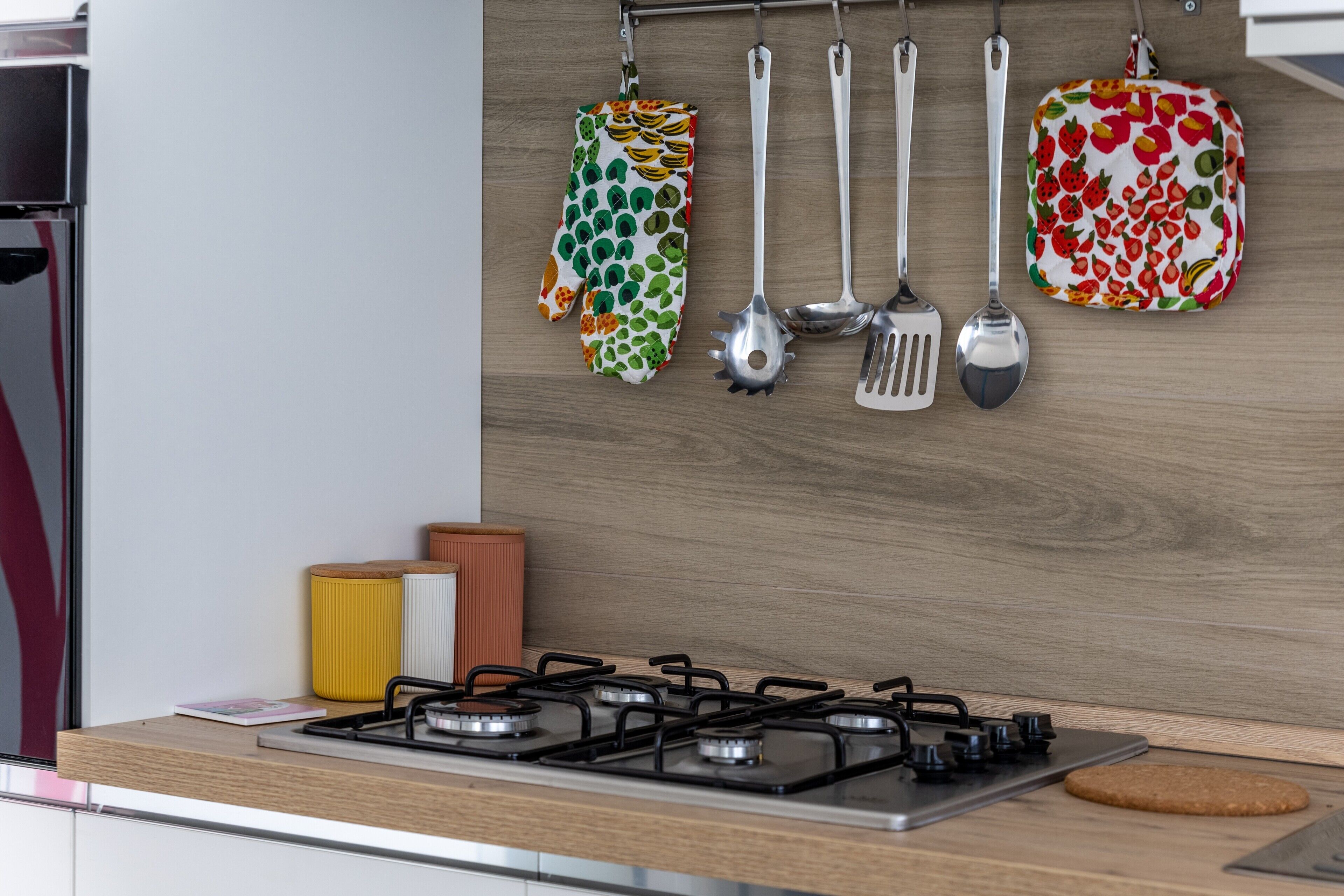 A kitchen with a gas stove, hanging utensils, and a wooden backsplash.