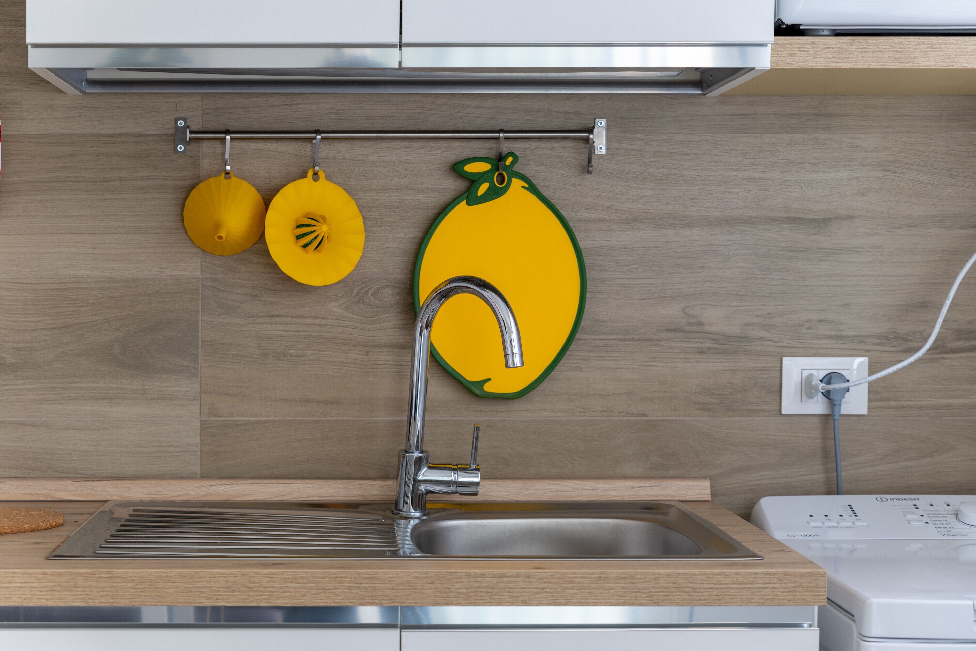 A modern kitchen with a stainless steel sink, wooden countertop, and a wall-mounted fruit-themed decoration.