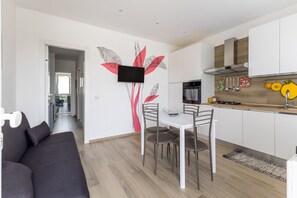 Eine moderne Küche mit weißen Schränken, einem flachbildfernseher an der Wand und einem Essbereich mit weißem Tisch und Stühlen.