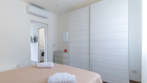 Un dormitorio con cama, lavadora, espejo y puerta corrediza.