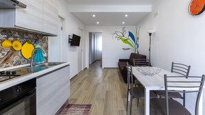 Una cocina moderna con horno empotrado, un comedor con mesa y sillas, y una sala de estar con sofá y televisor.