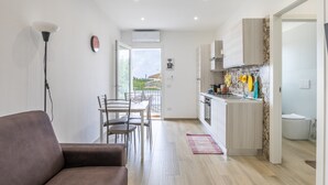 Una cocina moderna con armarios blancos, un comedor con sofá marrón y vistas a través de la puerta abierta.