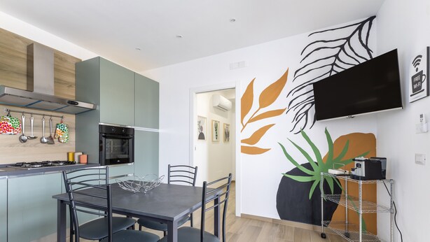 A modern kitchen with a dining area, a flat-screen TV mounted on the wall, and a wall art piece.