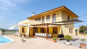 Una villa amarilla con piscina, mobiliario de exterior y zona de barbacoa.