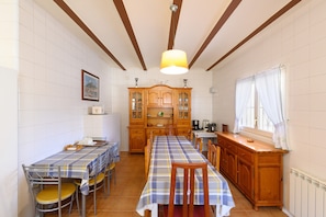 A dining area with a long table, chairs, a wooden cabinet, and a window with curtains.