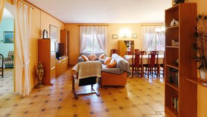 Una sala de estar con sofá, televisión, mesa de comedor, sillas y estantería.