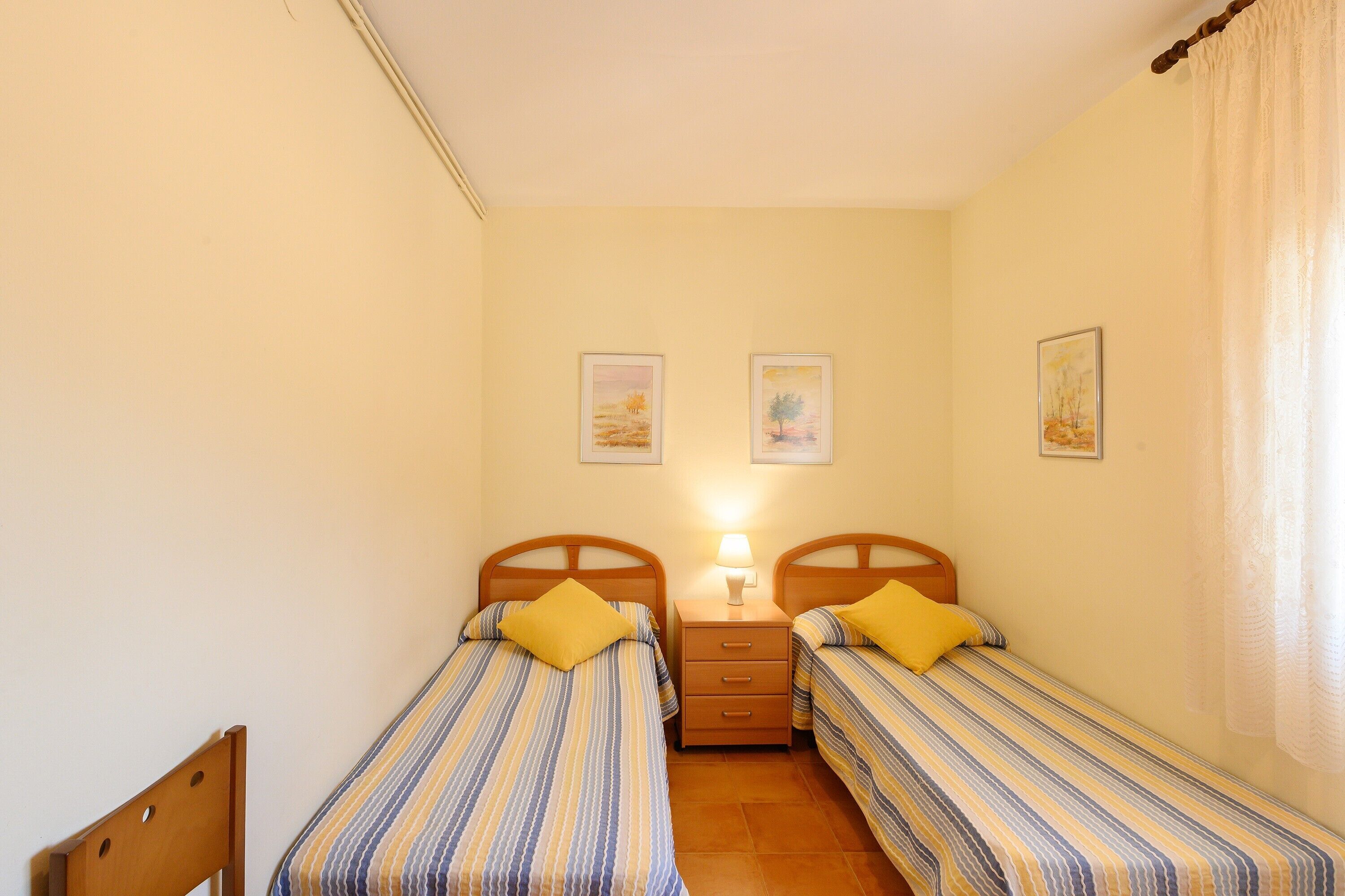 Ein Schlafzimmer mit zwei Einzelbetten, einem Nachttisch mit Lampe sowie zwei gerahmten Bildern an der Wand.