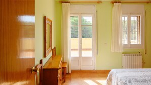 Una habitación con puerta de madera, una cama, un escritorio con silla, un radiador y una ventana con cortinas.