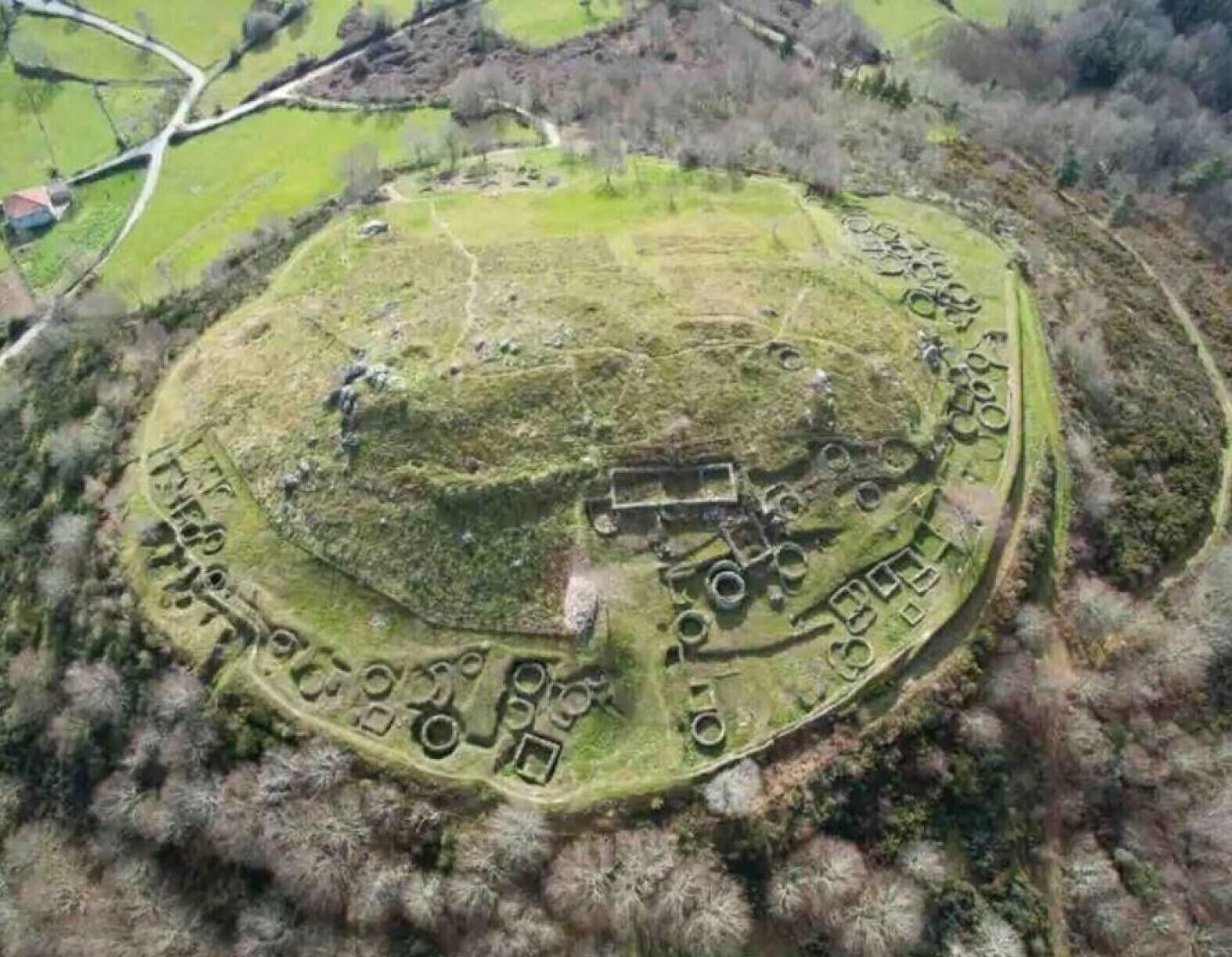 An aerial view of a historical site with a central mound, surrounding circular structures, and a rectangular building.