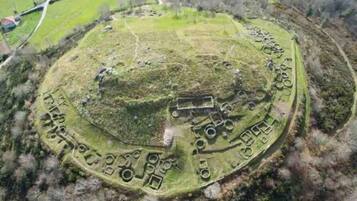 An aerial view of a historical site with a central mound, surrounding circular structures, and a rectangular building.