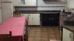 Una cocina compacta con armarios blancos, piso de baldosas, una mesa de comedor con sillas y una pequeña alfombra.