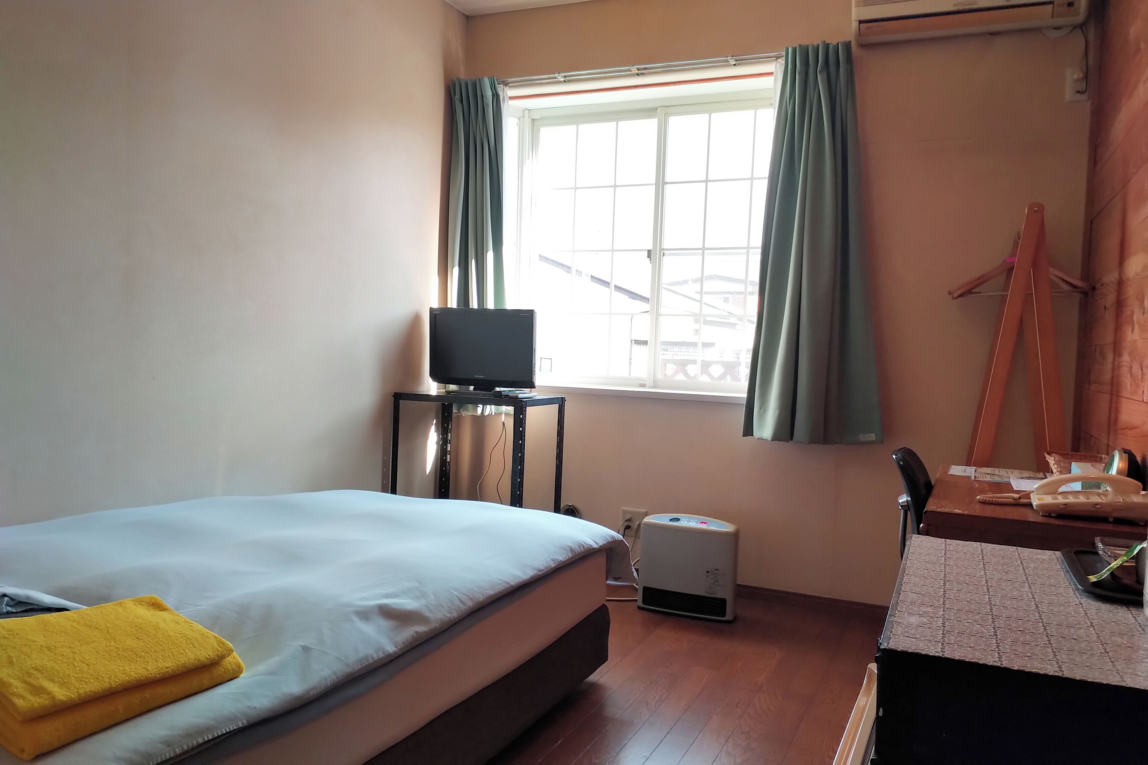 A hotel room with a bed, a desk with a telephone, a heater, and a window with curtains.
