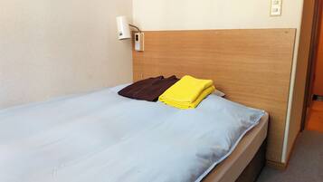 Una cama bien hecha con sábana azul claro, almohada marrón y toalla amarilla.