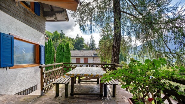 Un patio de piedra con una mesa y bancos de madera, rodeado de follaje y una valla de madera.