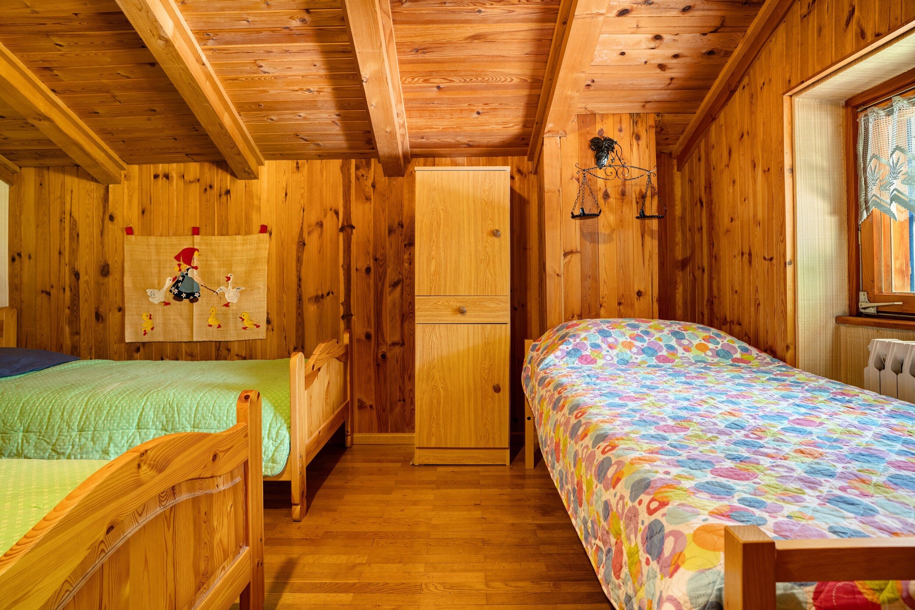Ein Schlafzimmer in einer Holzhütte mit zwei Betten, einem Kleiderschrank und einem Fenster mit Blick.