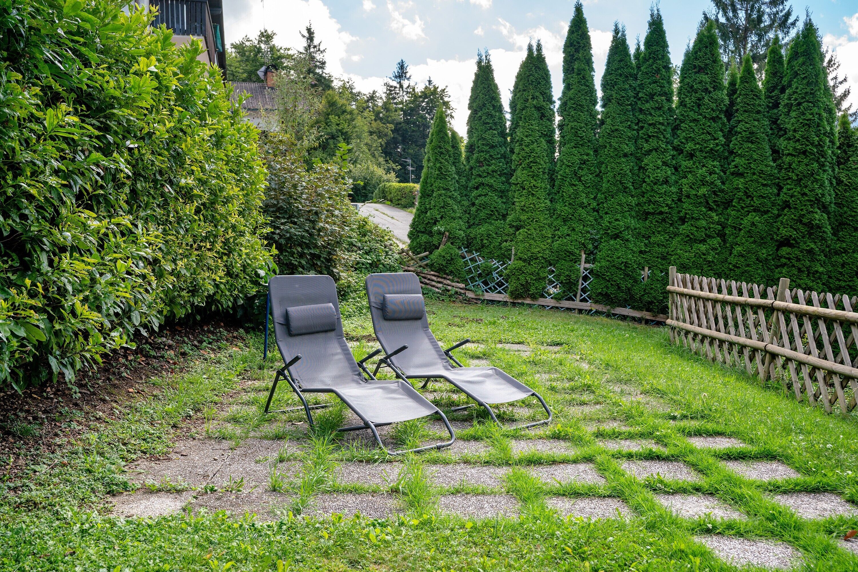 Dos sillones de jardín con una cerca de madera y árboles altos.