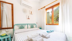 Une chambre à coucher comprenant un lit, une table de chevet, une fenêtre avec des rideaux et un climatiseur fixé au mur.
