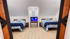 Une chambre avec deux lits, un bureau avec un ordinateur et une fenêtre avec des stores.