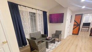 Un vaste salon doté d’un grand téléviseur à écran plat fixé au mur, d’un canapé, de deux fauteuils et d’une table basse.