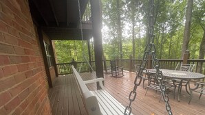 Une terrasse en bois avec une balançoire, des fauteuils à bascule et une table avec des chaises.