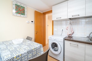 A compact kitchen with a washing machine, a clock, and a tiled backsplash. - Room 'Antares' with Shared Terrace, Wi-Fi and Air Conditioning (Avola)