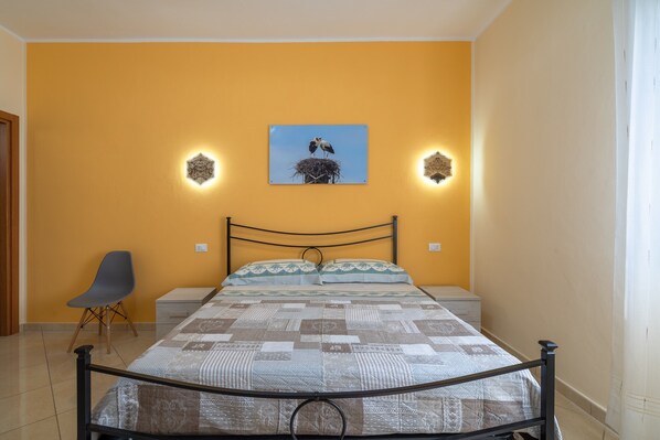 Une chambre à coucher comprenant un lit, une chaise, un tableau accroché au mur et deux appliques murales.