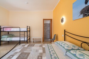 Une chambre avec des lits superposés, un banc, une chaise, un tableau et une porte donnant sur une salle de bain.