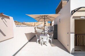 Une terrasse avec une table et des chaises, un grand parasol et une vue sur un bâtiment en arrière-plan.