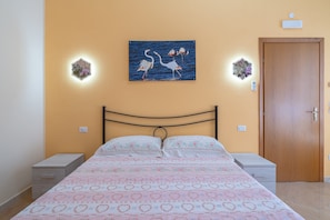 A bedroom with a bed, two bedside tables, a wooden door, and wall-mounted lights. - Room 'Sirius' with Shared Terrace, Wi-Fi and Air Conditioning (Avola)