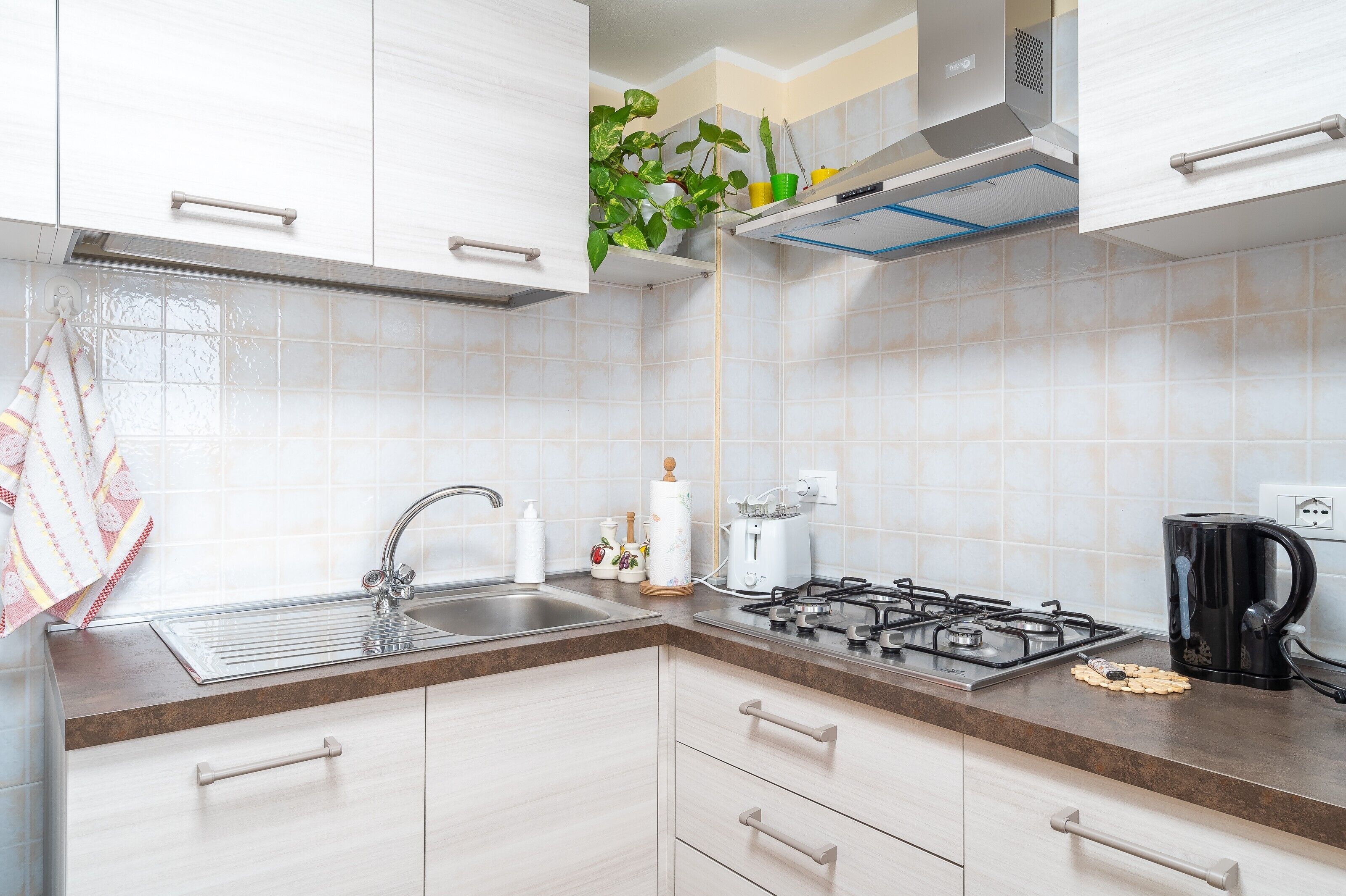 A kitchen with white cabinets, a stainless steel sink, a gas stove, and a coffee maker.
