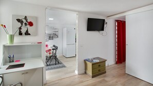 A room with a desk, a television, a small cabinet, and a door leading to another room.
