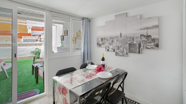 A dining area with a table set for two, a cityscape wall art, and a sliding glass door leading to an outdoor space with a green lawn.