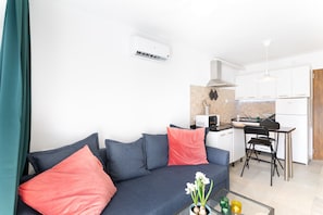 Ein modernes Wohnzimmer mit einer Couch, einem Glastisch und einer Küchenzeile mit Mikrowelle und Herd.
