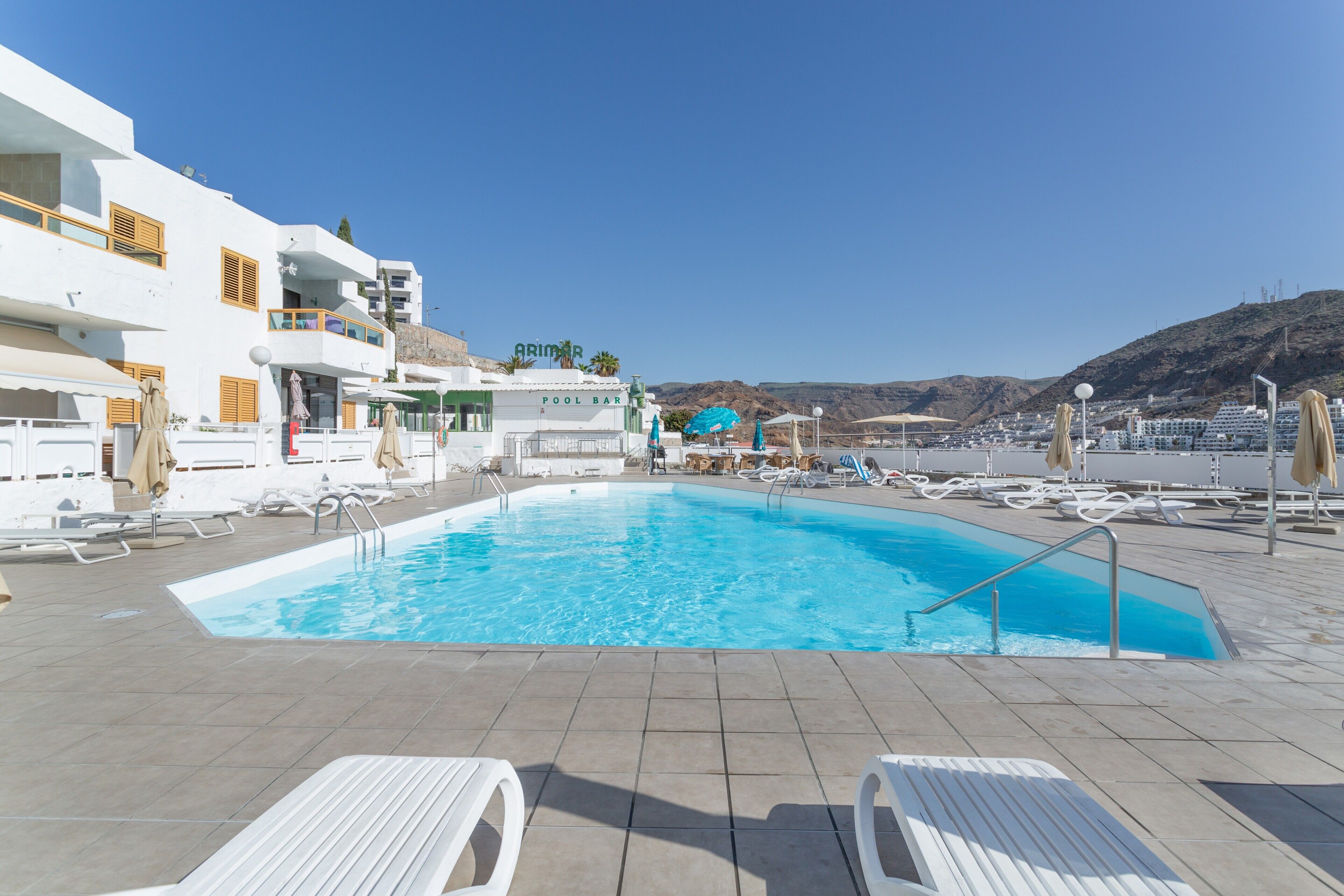 A pool area with lounge chairs, a pool bar, and a view of the surrounding landscape.