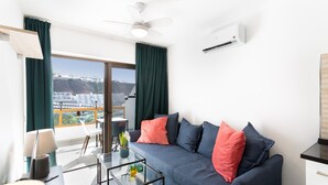 A modern living room with a sofa, a glass coffee table, a ceiling fan, and a view of a cityscape through a large window. - Vacation Home 'Casa Neale' with Sea View, Shared Pool and Private Terrace (Puerto Rico)