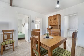 Een eetgedeelte met een houten tafel en stoelen, een keuken met witte kasten, en een badkamer met een witte bakstenen muur.