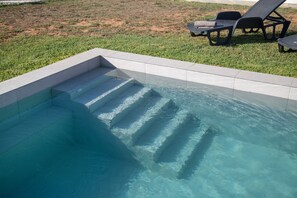 A swimming pool with clear water, steps leading into it, and two lounge chairs on the grass. - Holiday Home 'Casa Rural La Ferrera' with Private Pool, Wi-Fi and Air Conditioning (Chiclana de la Frontera)