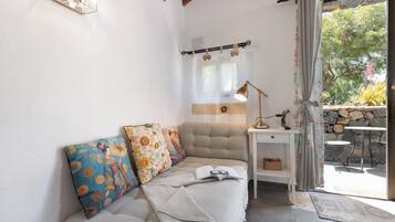 Et hyggeligt værelse med sofa, puder, et lille bord, en lampe og udsigt til det fri.