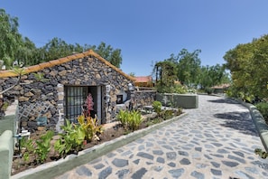 Un bâtiment en pierre avec un toit en tuiles, un chemin pavé et diverses plantes.