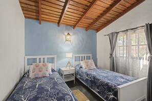 A bedroom with two beds, a nightstand, a wall-mounted lamp, and a window with curtains.