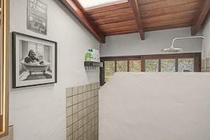 A bathroom with a shower, a framed photograph on the wall, and a shelf with toiletries.