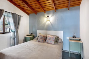 Ein Schlafzimmer mit einem Bett, einem Nachttisch, einer Lampe und einem Fenster mit Vorhängen.