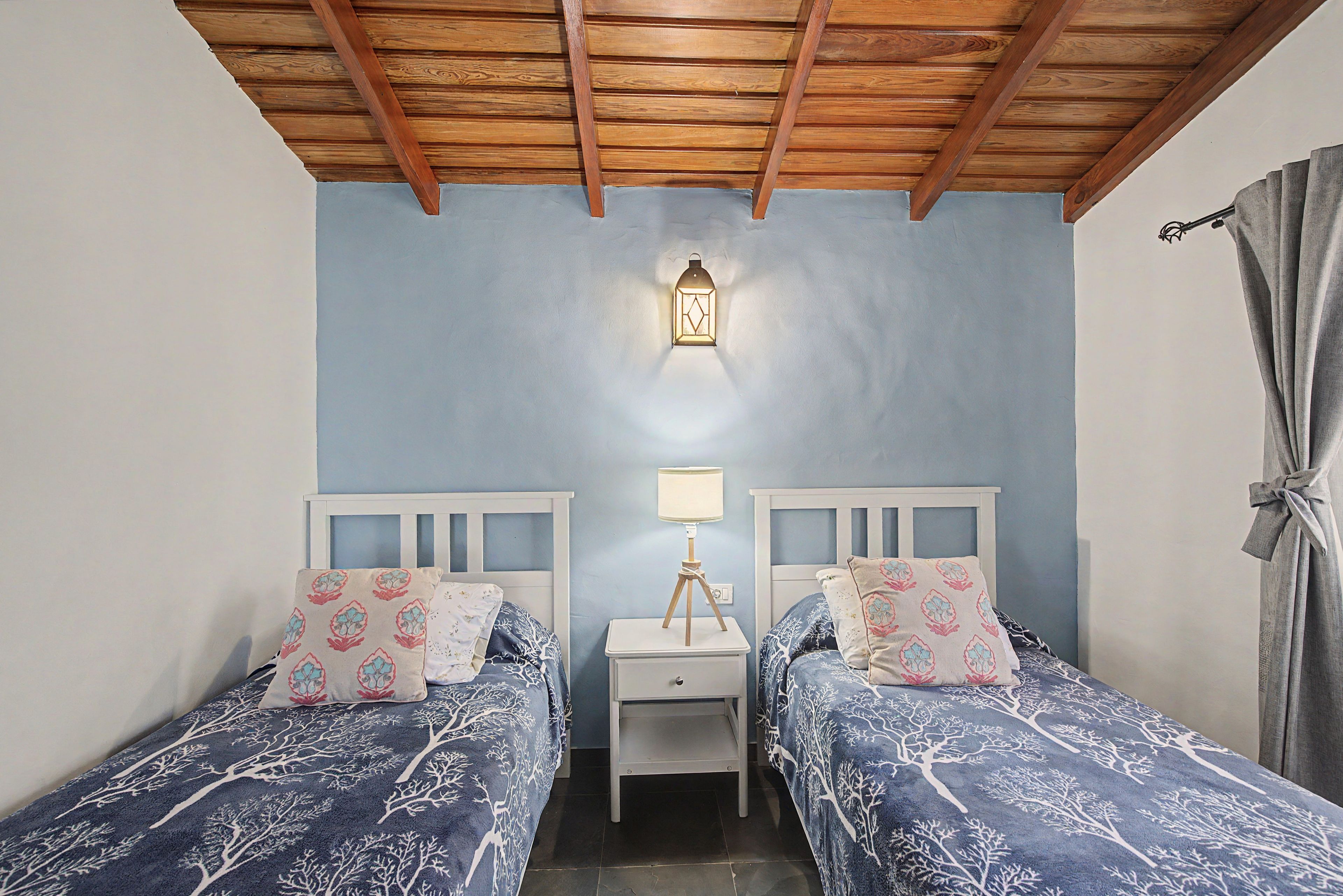Una camera da letto con due letti, un comodino, una lampada a parete e un soffitto in legno.