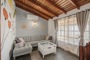 A living room with a sectional sofa, a white coffee table, and a large window with floral curtains.