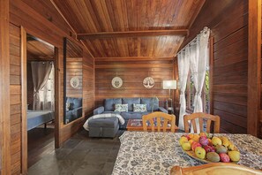 A cozy cabin interior with a wooden ceiling, a sofa set, a dining table with fruit, and a mirror reflecting the room.