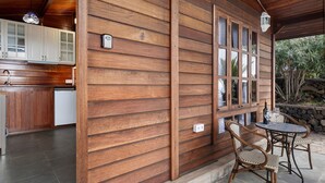 A wooden exterior wall with a window, a kitchen area with cabinets, and a dining table with chairs.