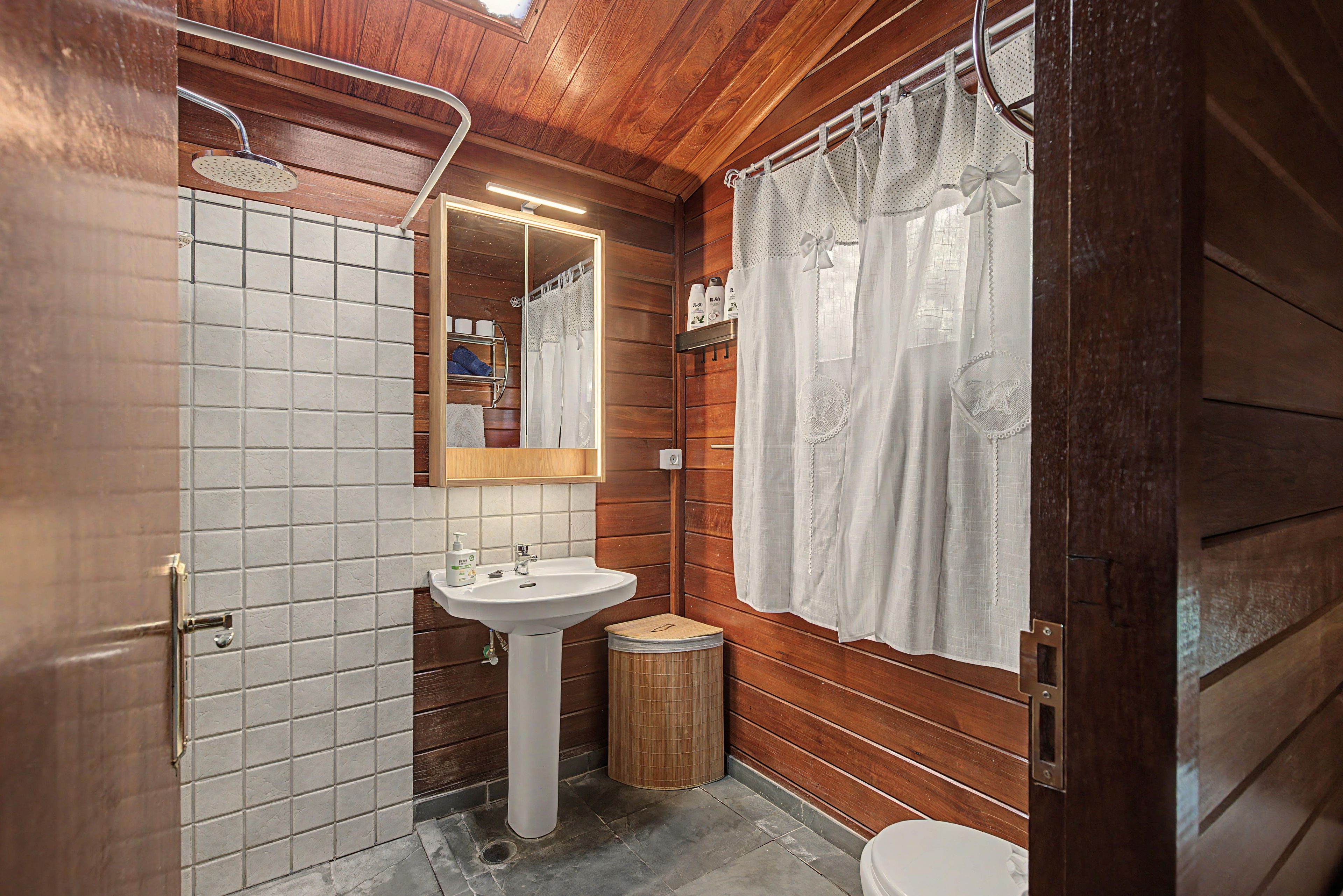 Een badkamer met een houten inrichting, een witte wastafel, een spiegel en een douche.
